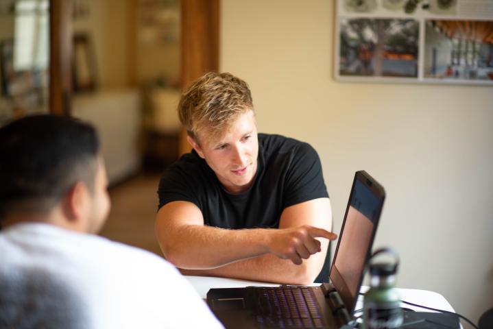 A blonde male student points at a computer in the Career Services office as he speaks with another student during a career advising appointment.
